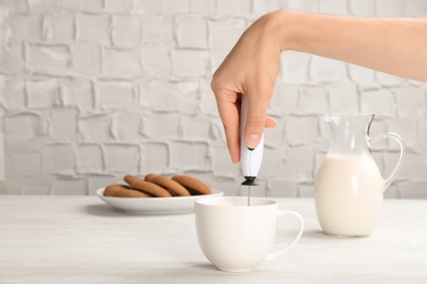Photo of Woman using milk frother device in cup on table