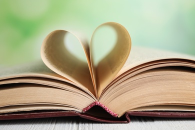 Open book on white wooden table against blurred green background, closeup