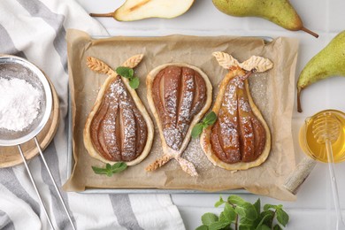 Delicious pears baked in puff pastry with powdered sugar served on white table, flat lay