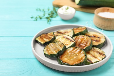 Photo of Plate of delicious grilled zucchini slices on light blue wooden table. Space for text