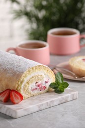 Photo of Delicious sponge cake roll with strawberries and cream on light grey table, space for text