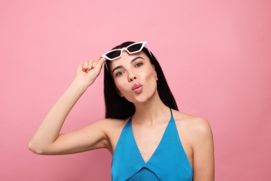 Beautiful young woman blowing kiss on pink background