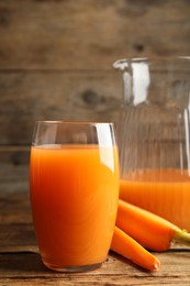 Photo of Jug and glass of freshly made carrot juice on wooden table