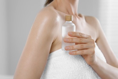 Woman with bottle of body oil on light grey background, closeup