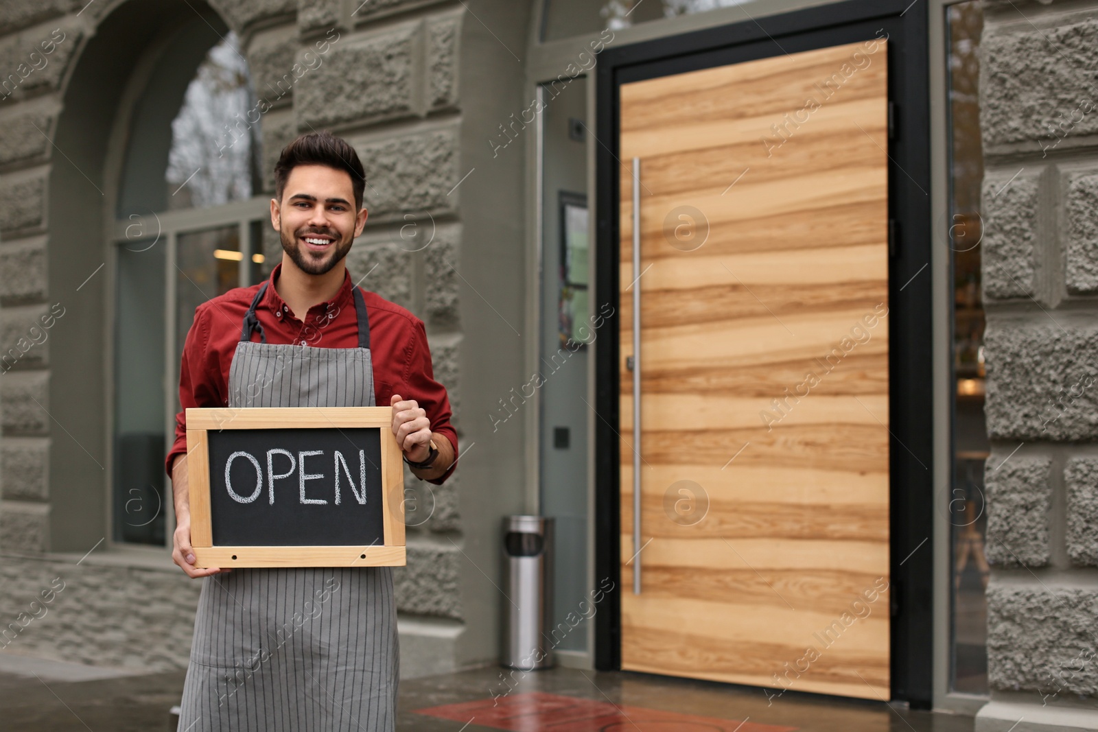 Photo of Young male business owner holding OPEN sign near his cafe. Space for text