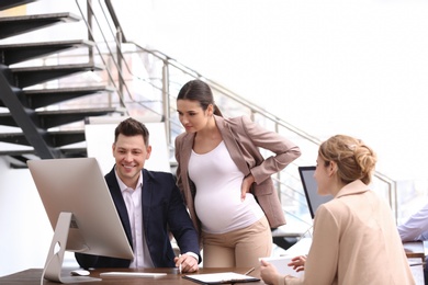 Young pregnant woman working with her employees in office