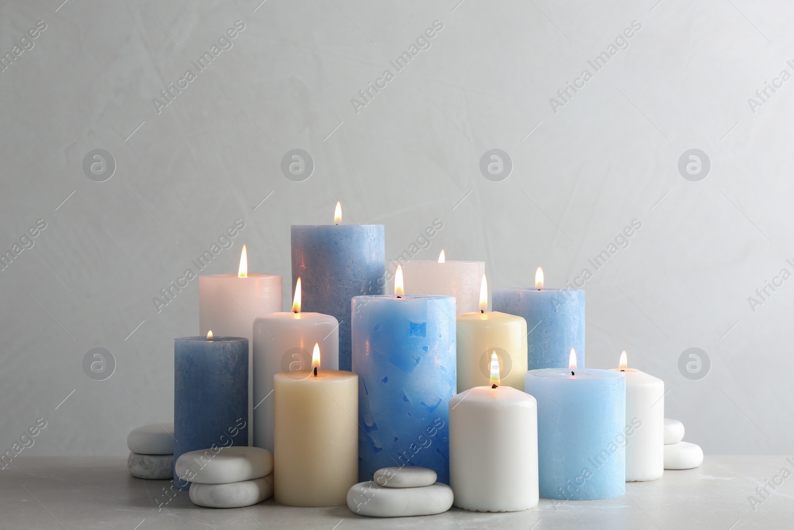 Photo of Composition with burning candles on table against light background