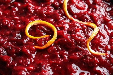 Tasty cranberry sauce with citrus zest as background, closeup