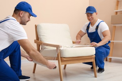 Workers wrapping armchair in stretch film indoors