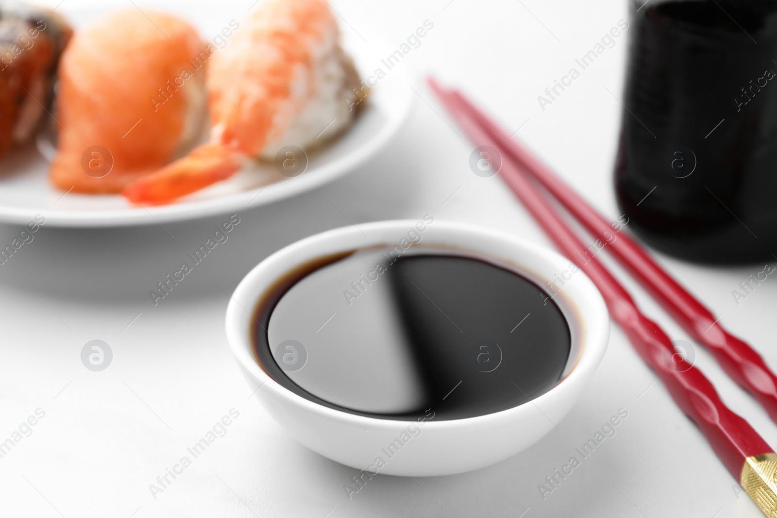 Photo of Tasty soy sauce, chopsticks and different types of sushi on white table, closeup