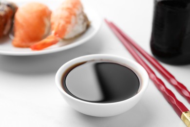 Photo of Tasty soy sauce, chopsticks and different types of sushi on white table, closeup