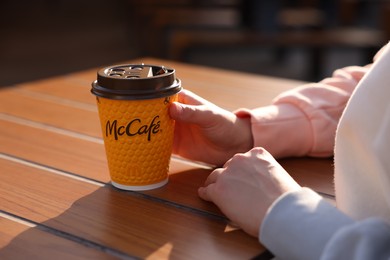 Photo of Lviv, Ukraine - September 26, 2023: Woman with hot McDonald's drink at wooden table outdoors, closeup