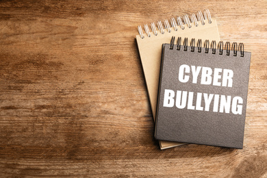 Image of Stylish notebooks with phrase CYBER BULLYING on wooden table, top view. Space for text