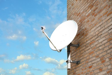 Satellite dish on brick wall of building against blue sky