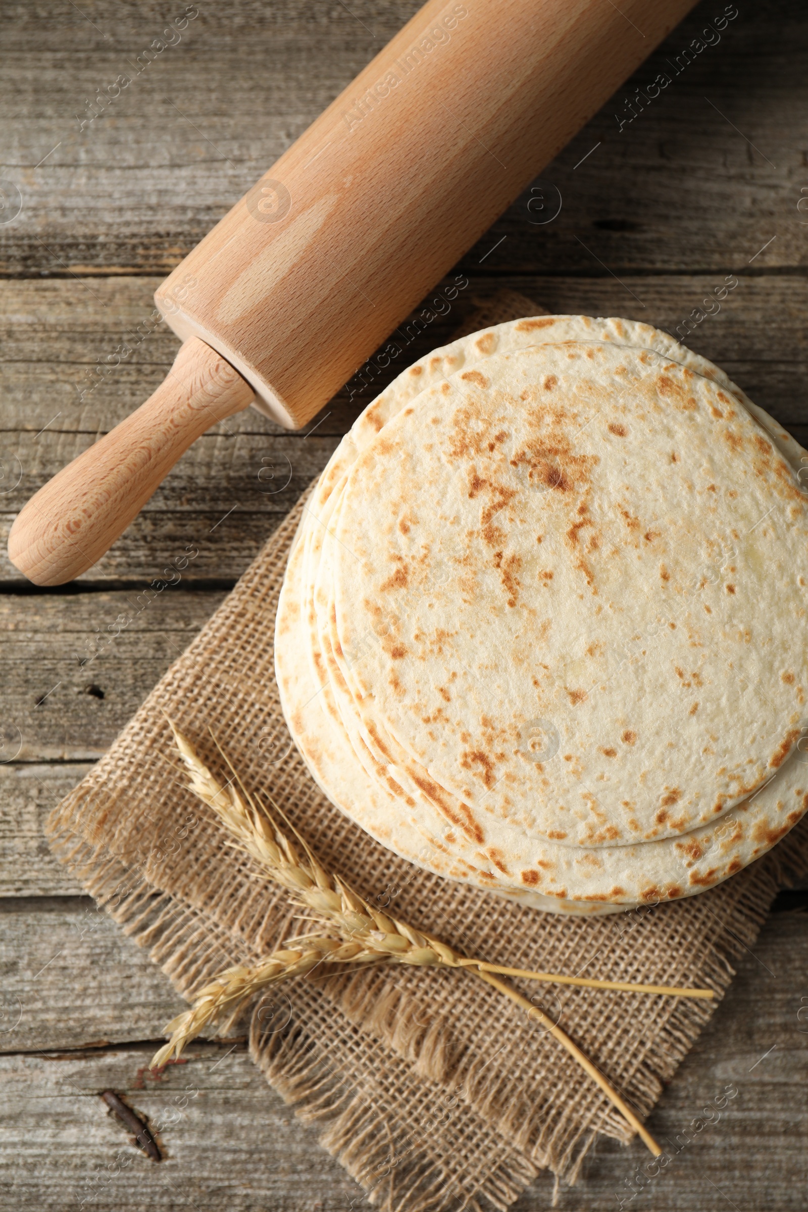 Photo of Tasty homemade tortillas, rolling pin and spikes on wooden table, top view