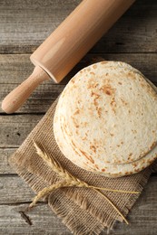 Tasty homemade tortillas, rolling pin and spikes on wooden table, top view