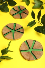 Photo of Stylish wooden cup coasters and green leaves on yellow background