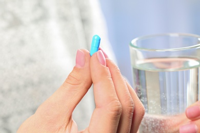 Woman holding pill and glass of water on blurred background, closeup