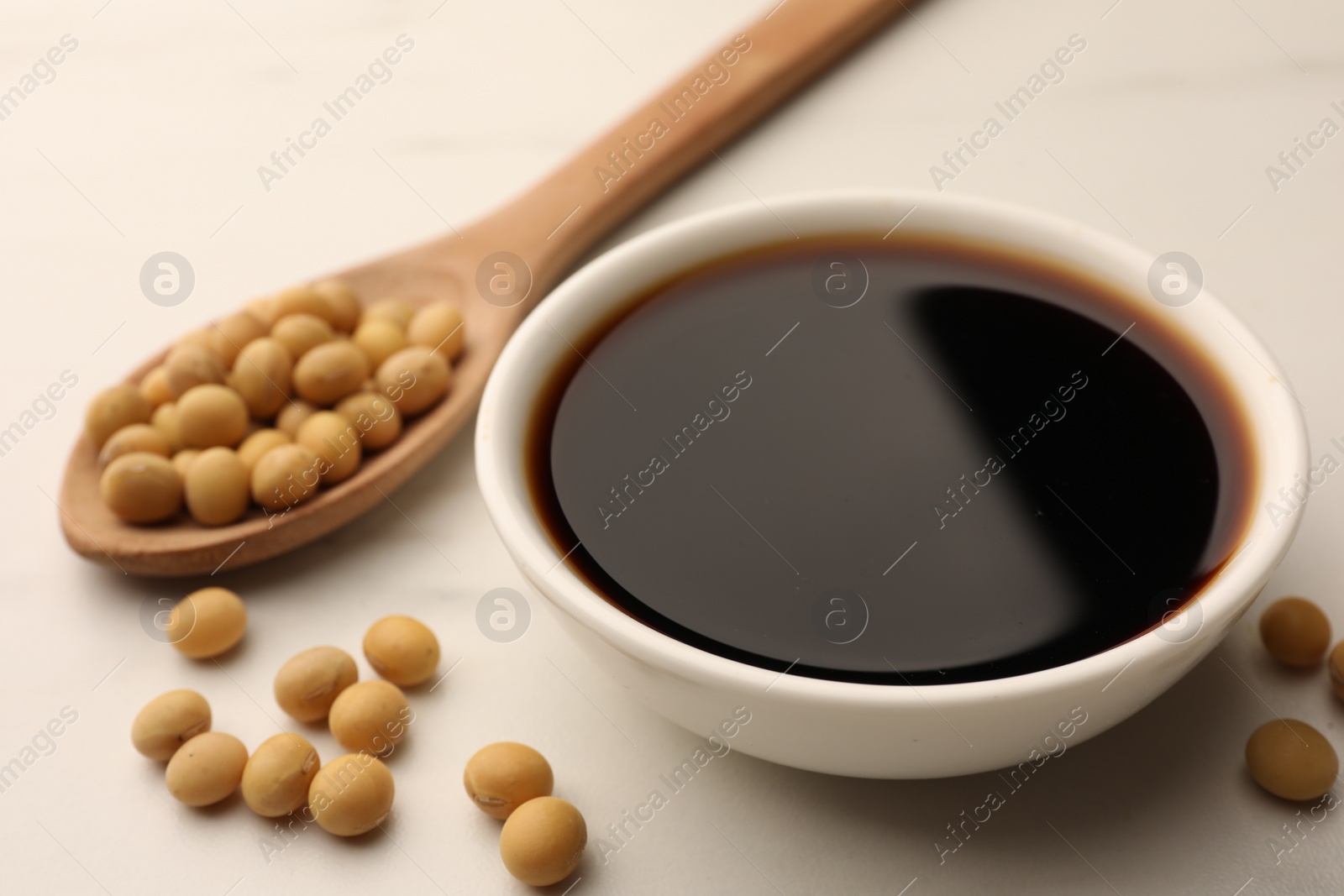 Photo of Soy sauce in bowl and soybeans on white table, closeup