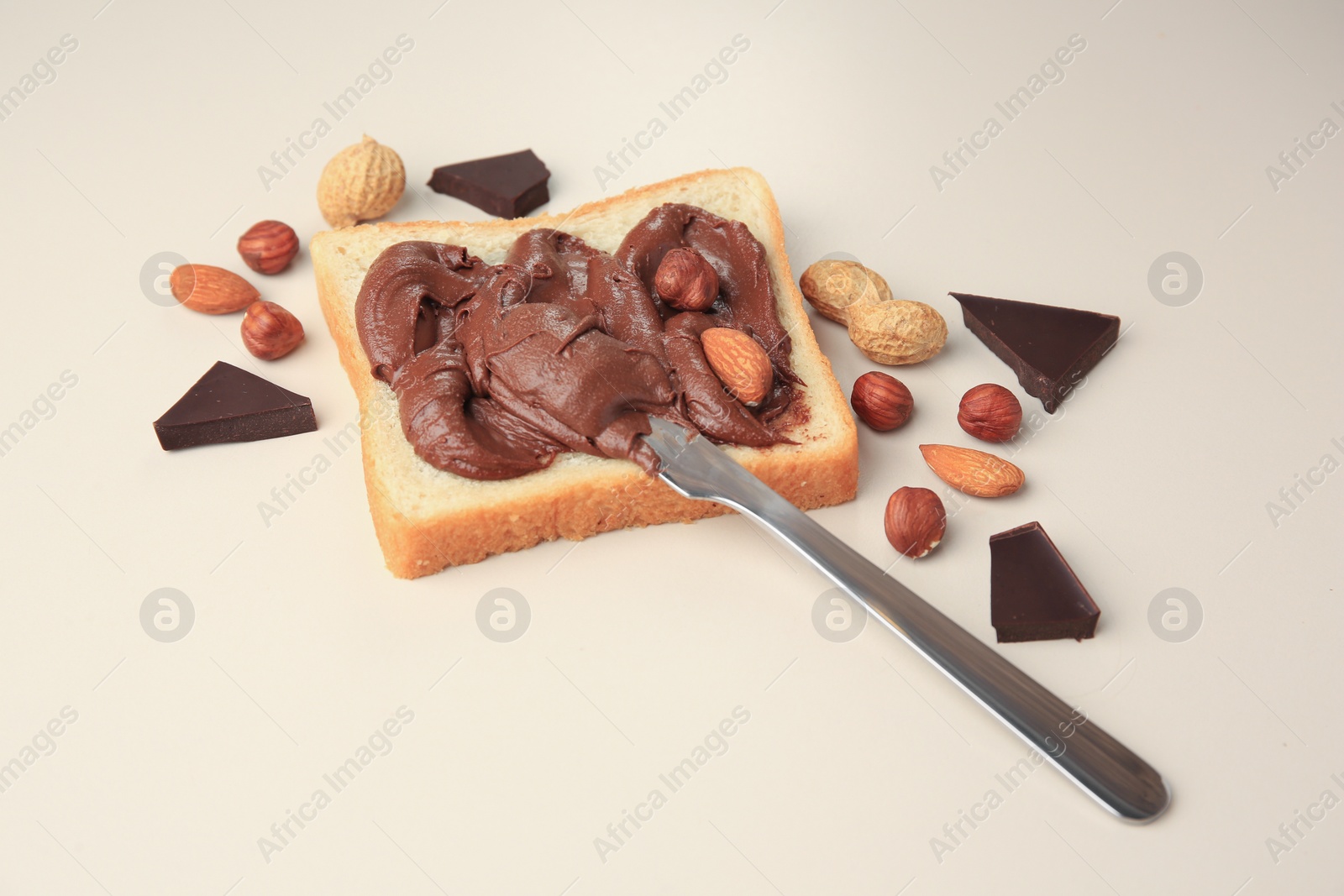 Photo of Tasty toast with chocolate paste and nuts on beige background