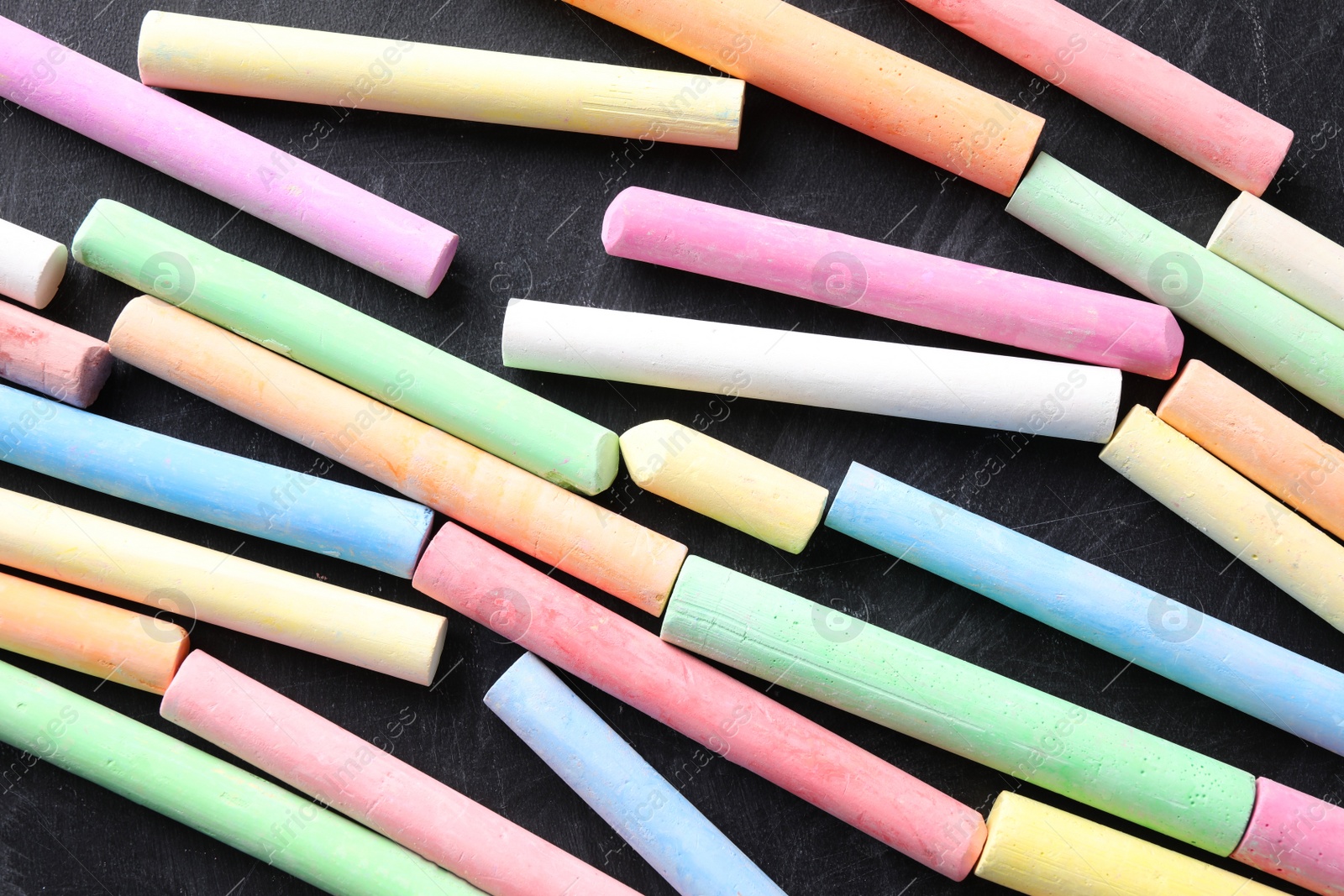 Photo of Pieces of color chalk on blackboard, flat lay