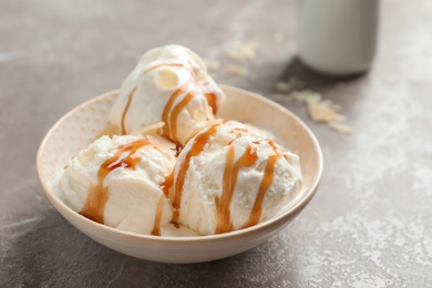 Tasty ice cream with caramel sauce in bowl on table