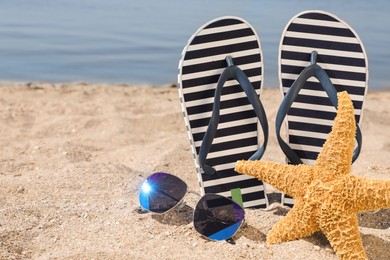 Stylish flip flops, sunglasses and starfish on sandy beach, space for text