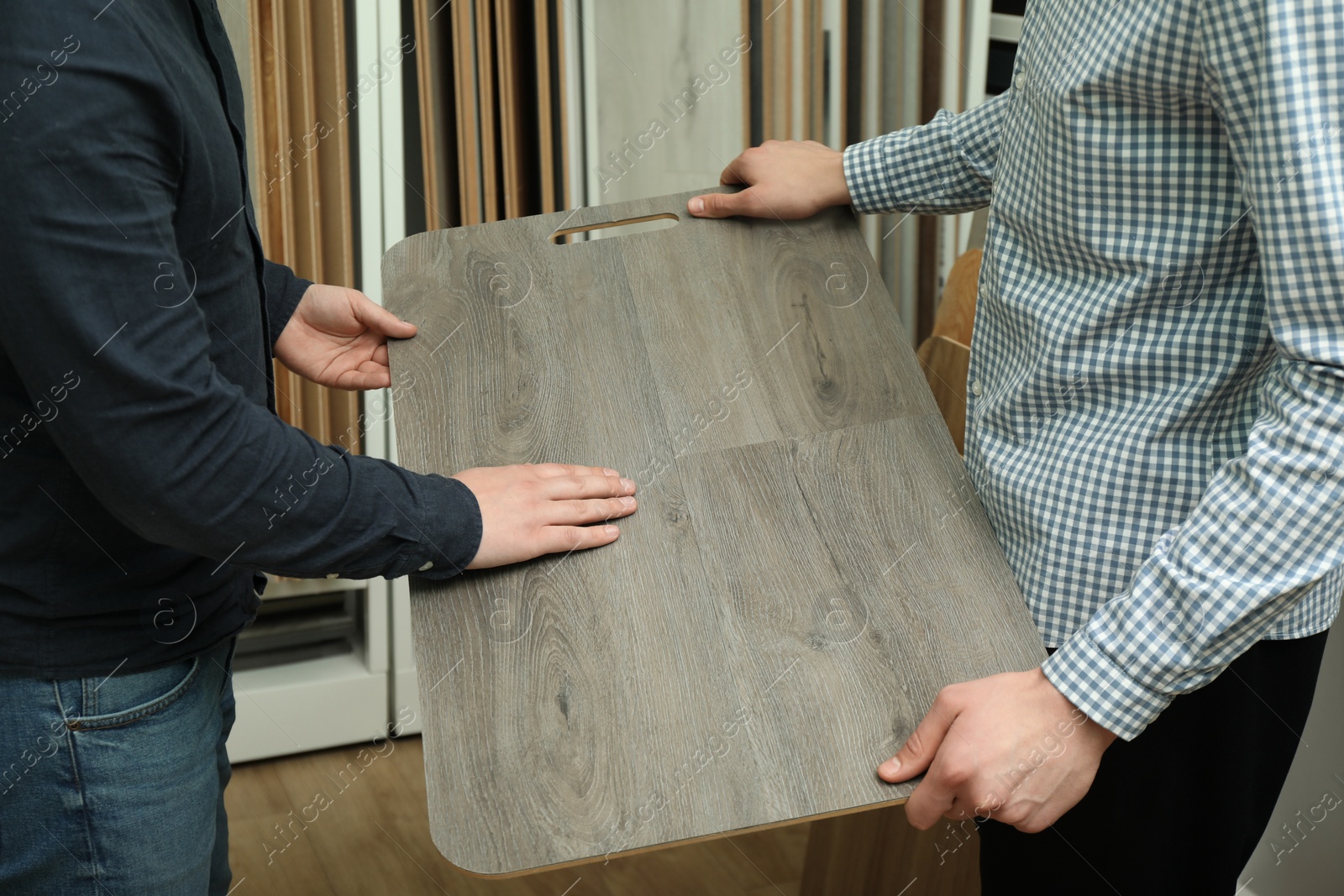 Photo of Men holding sample of wooden flooring in shop, closeup