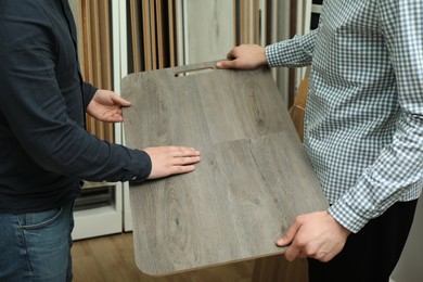 Men holding sample of wooden flooring in shop, closeup