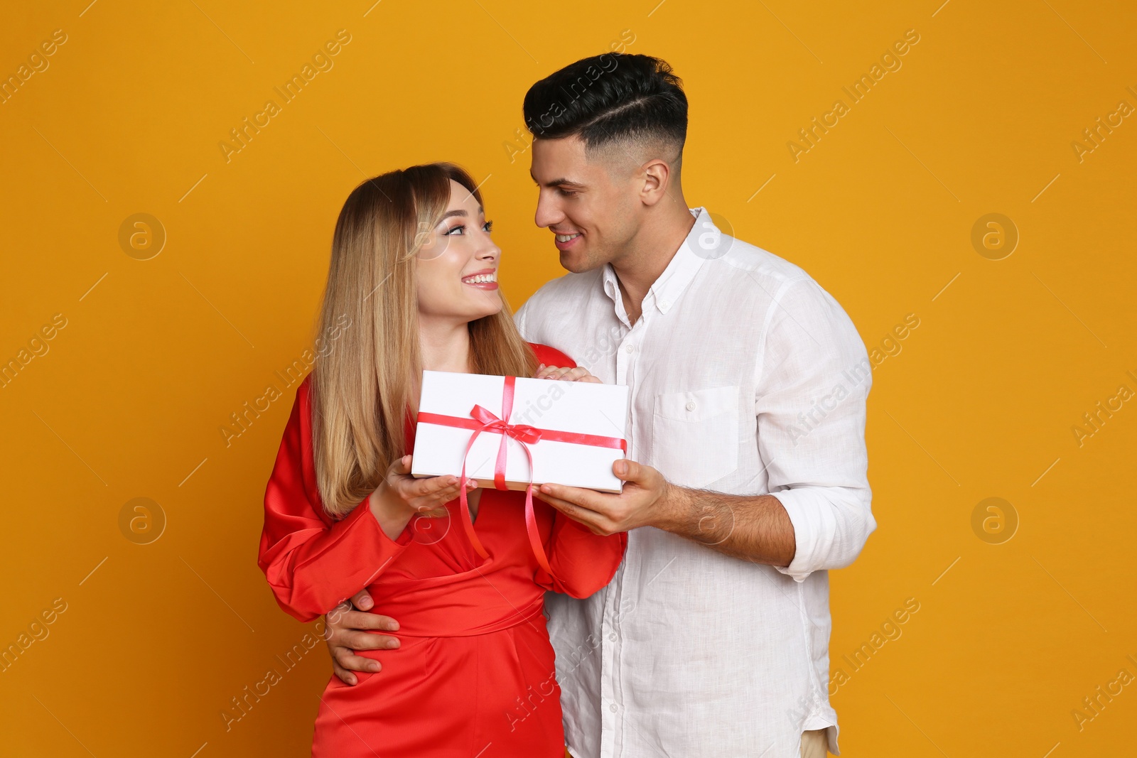 Photo of Lovely couple with gift on yellow background. Valentine's day celebration