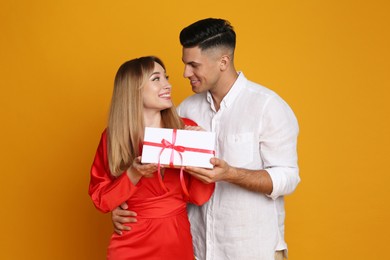 Photo of Lovely couple with gift on yellow background. Valentine's day celebration