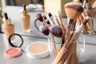 Photo of Set of professional brushes and makeup products near mirror on grey table, closeup. Space for text