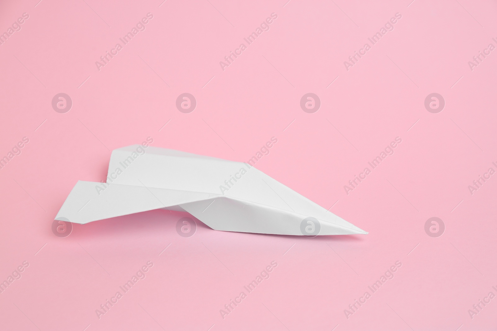 Photo of White paper plane on pink background, space for text