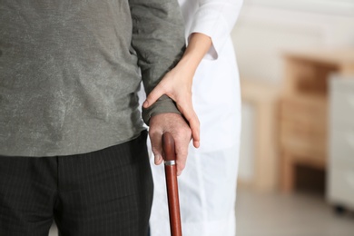 Photo of Elderly man with walking cane and female caregiver on blurred background, closeup view. Space for text