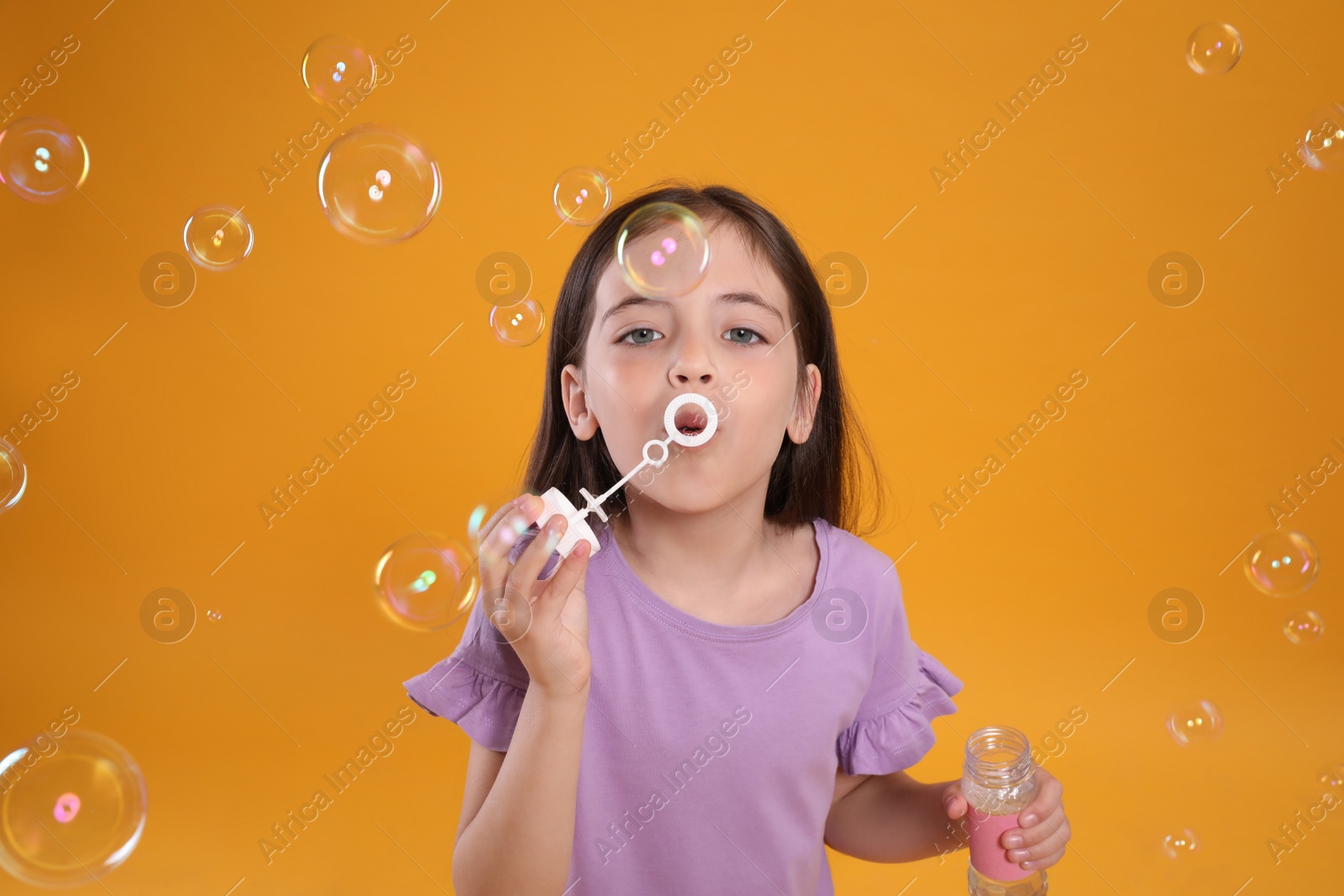 Photo of Little girl blowing soap bubbles on yellow background