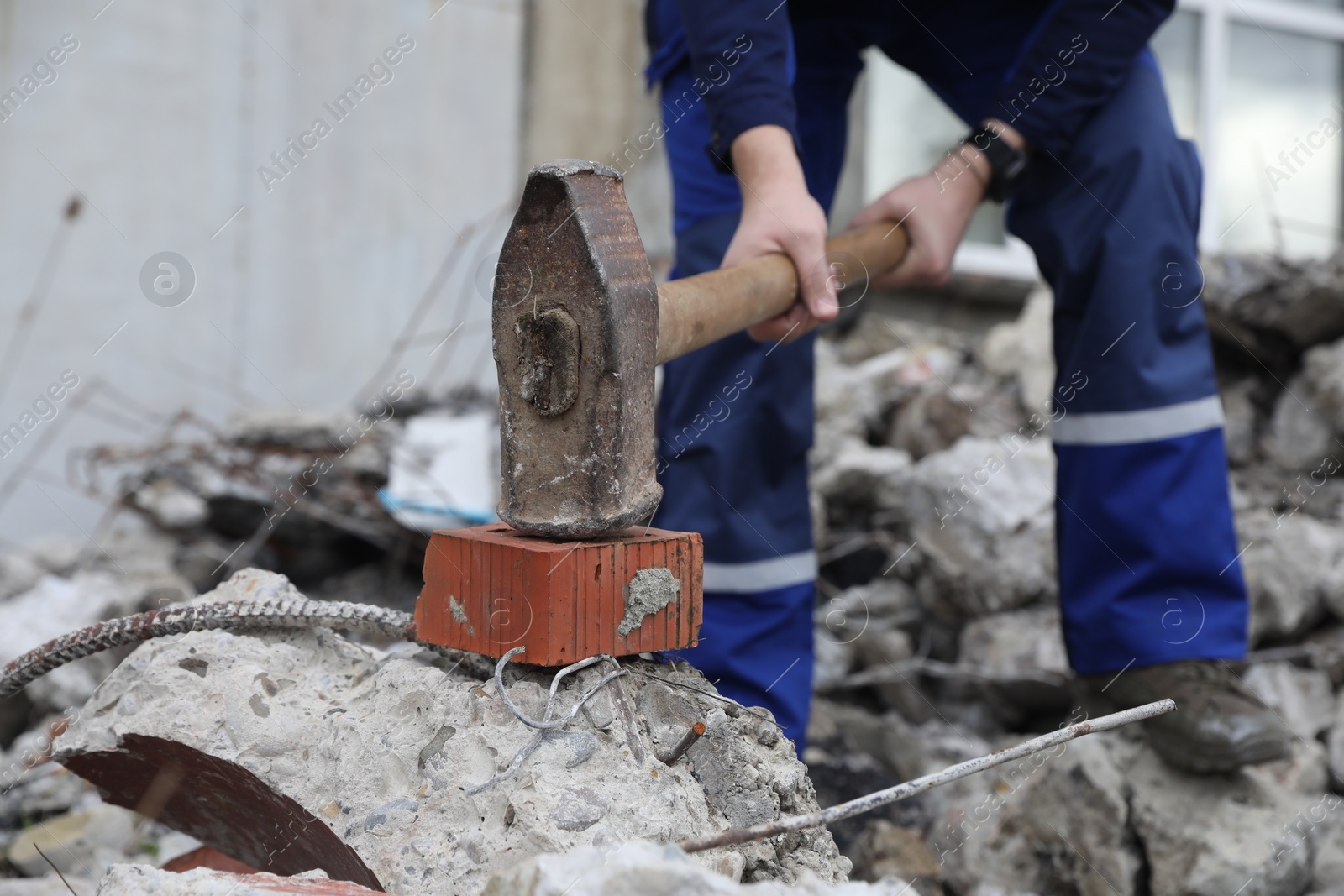 Photo of Man breaking brick with sledgehammer outdoors, selective focus