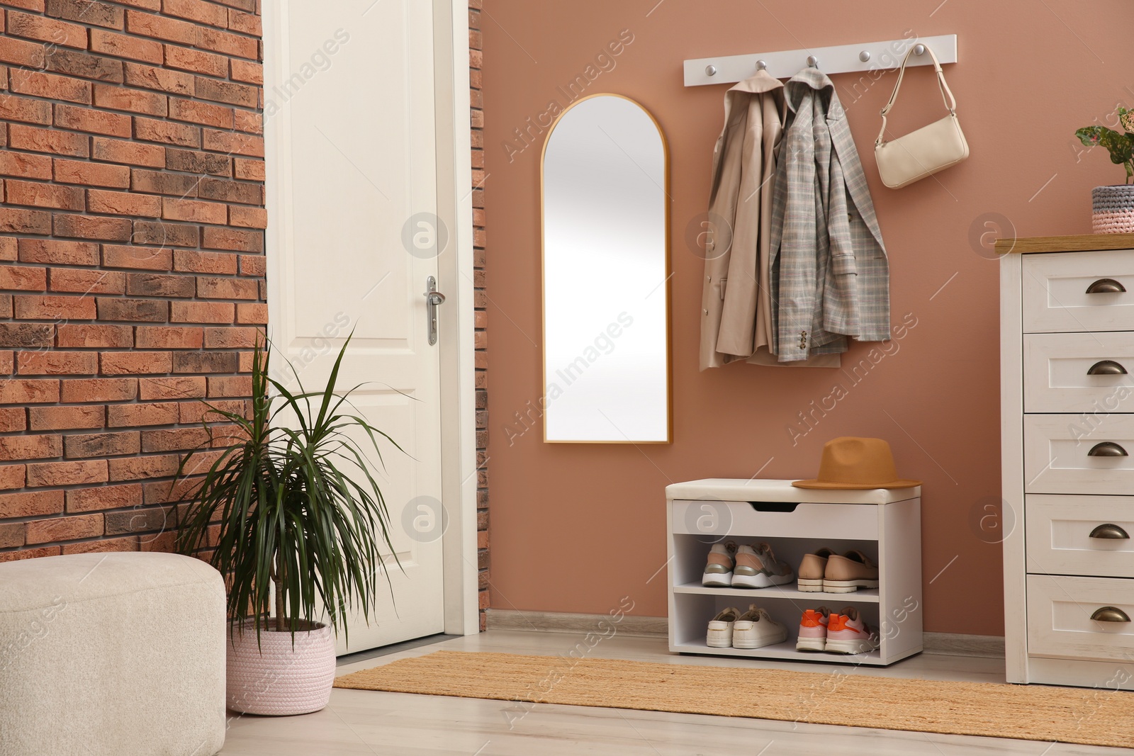 Photo of Rack with different shoes near pale pink wall in hall