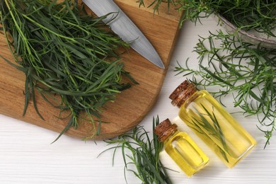 Photo of Bottles of essential oil and fresh tarragon sprigs on white wooden table, flat lay