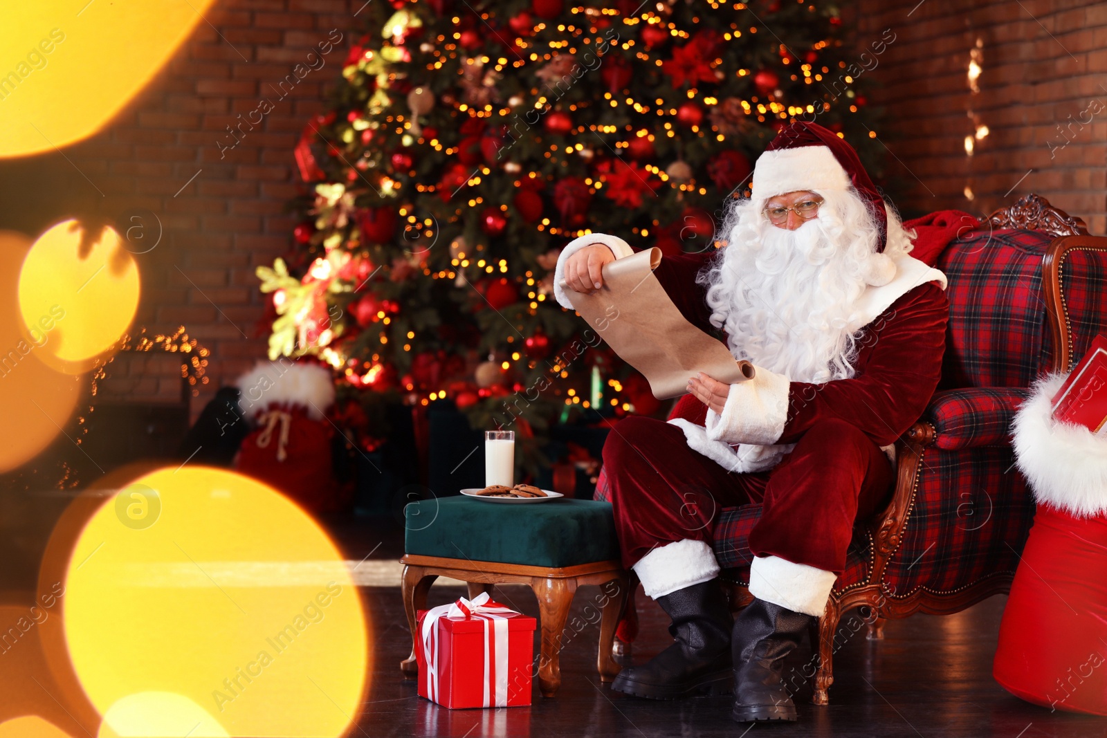 Photo of Santa Claus with wish list near Christmas tree indoors