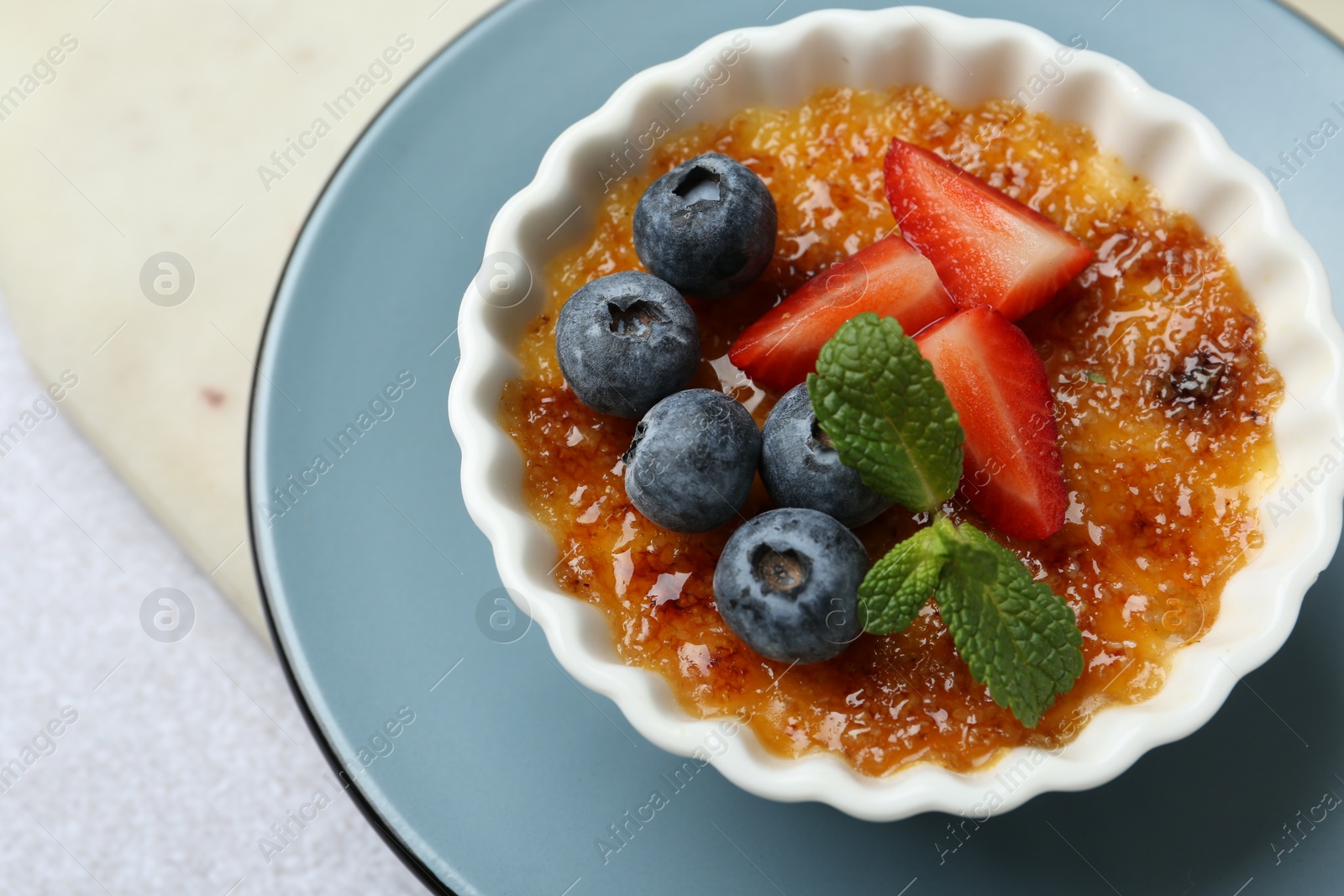 Photo of Delicious creme brulee with berries and mint in bowl on grey table, above view