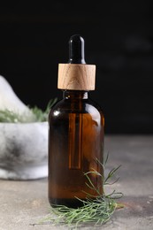 Photo of Bottle of essential oil and fresh dill on light gray textured table, closeup