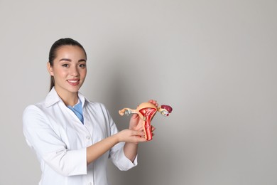 Photo of Doctor demonstrating model of female reproductive system on light grey background, space for text. Gynecological care
