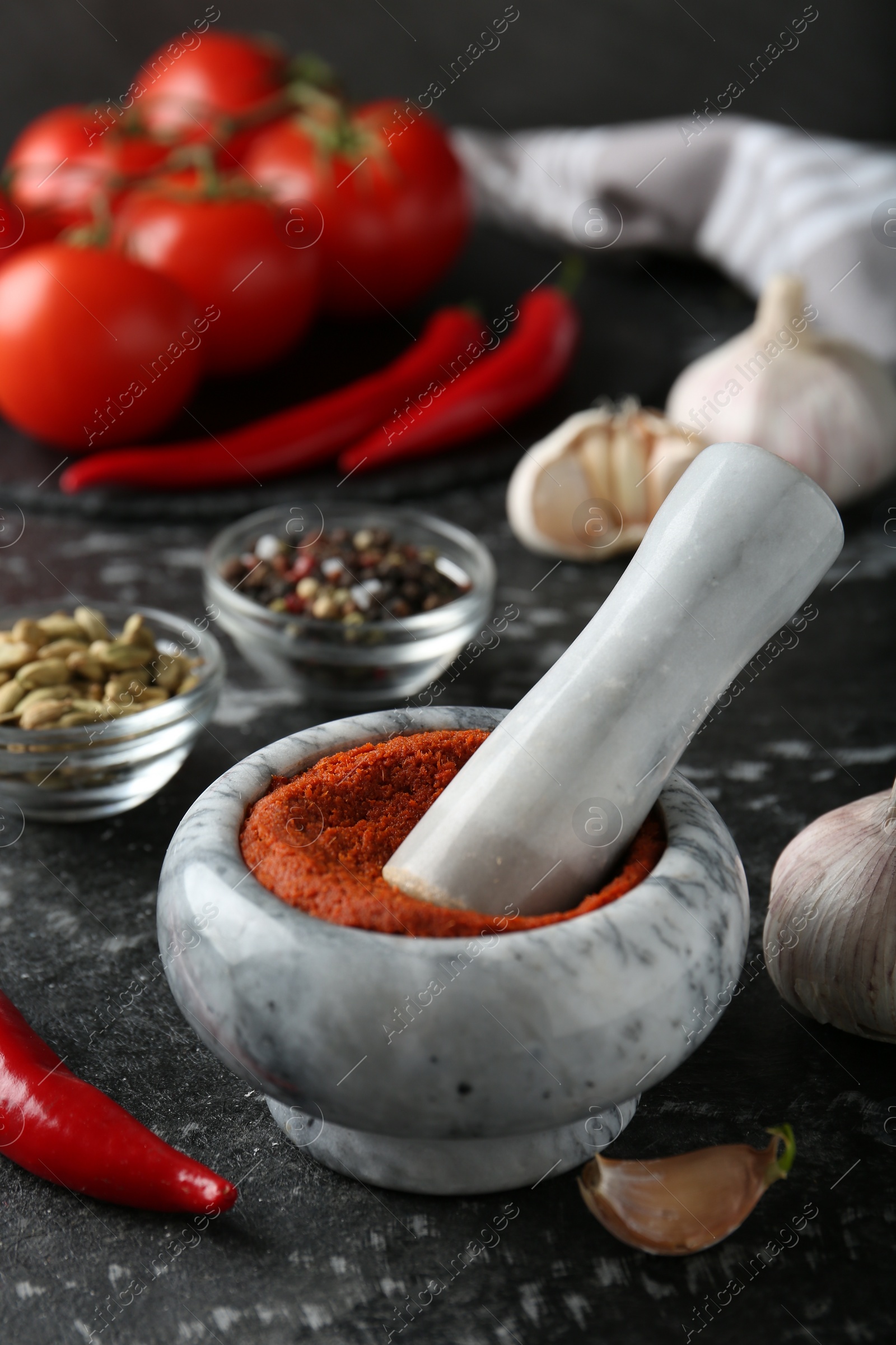 Photo of Mortar with red curry paste and ingredients on black textured table