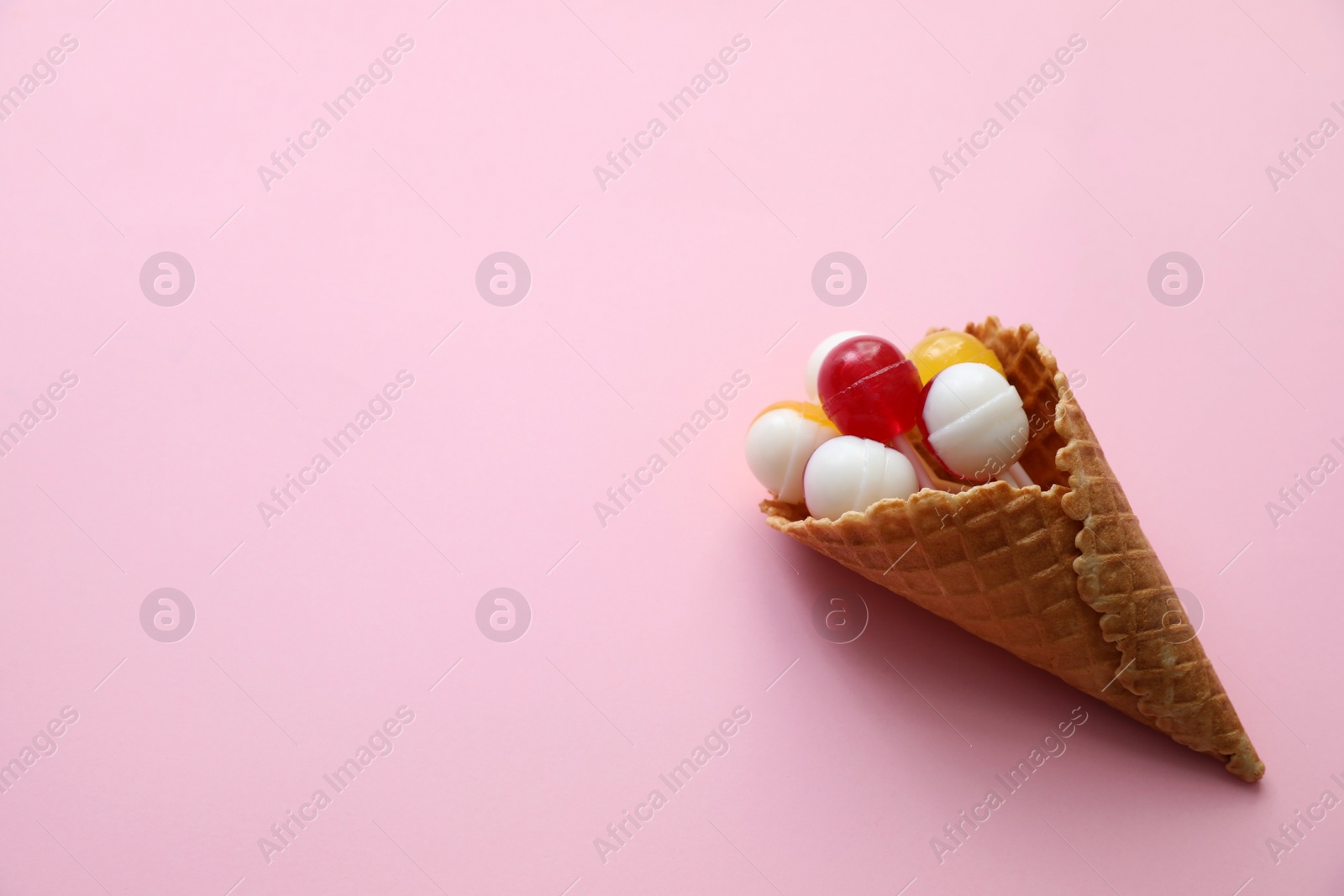 Photo of Delicious lollipop candies in wafer cone on pink background, top view. Space for text