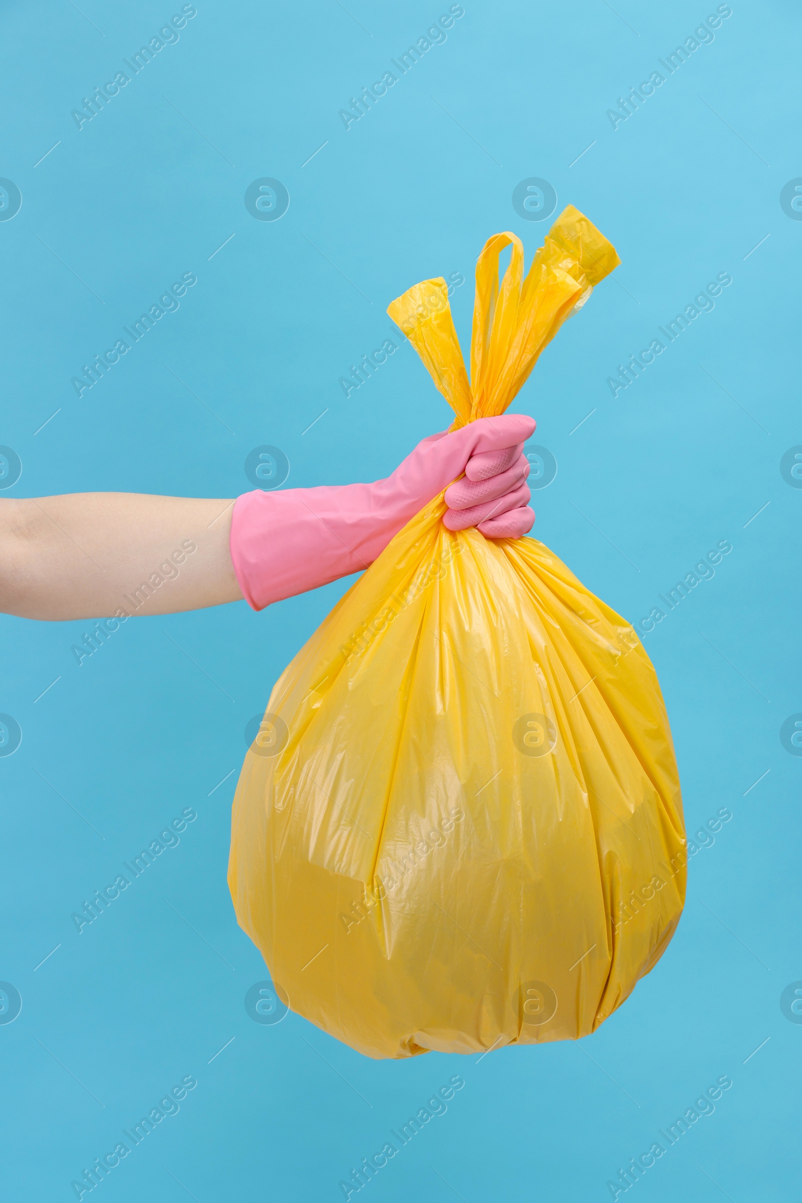 Photo of Woman holding plastic bag full of garbage on light blue background, closeup