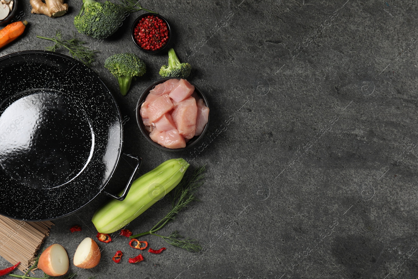 Photo of Empty iron wok surrounded by ingredients on grey table, flat lay. Space for text