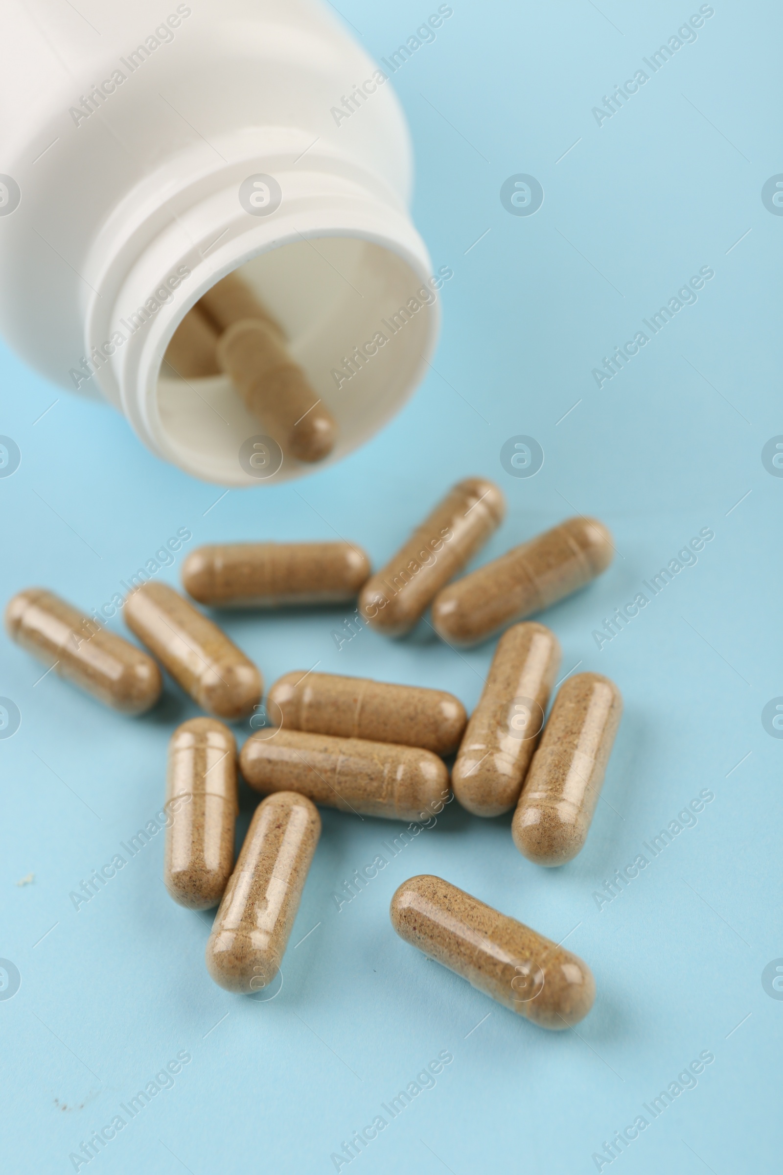 Photo of Bottle and vitamin capsules on light blue background, closeup