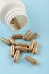 Bottle and vitamin capsules on light blue background, closeup