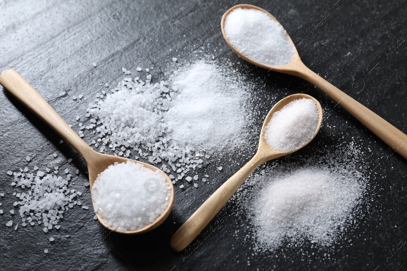 Photo of Organic salt in spoons on black table