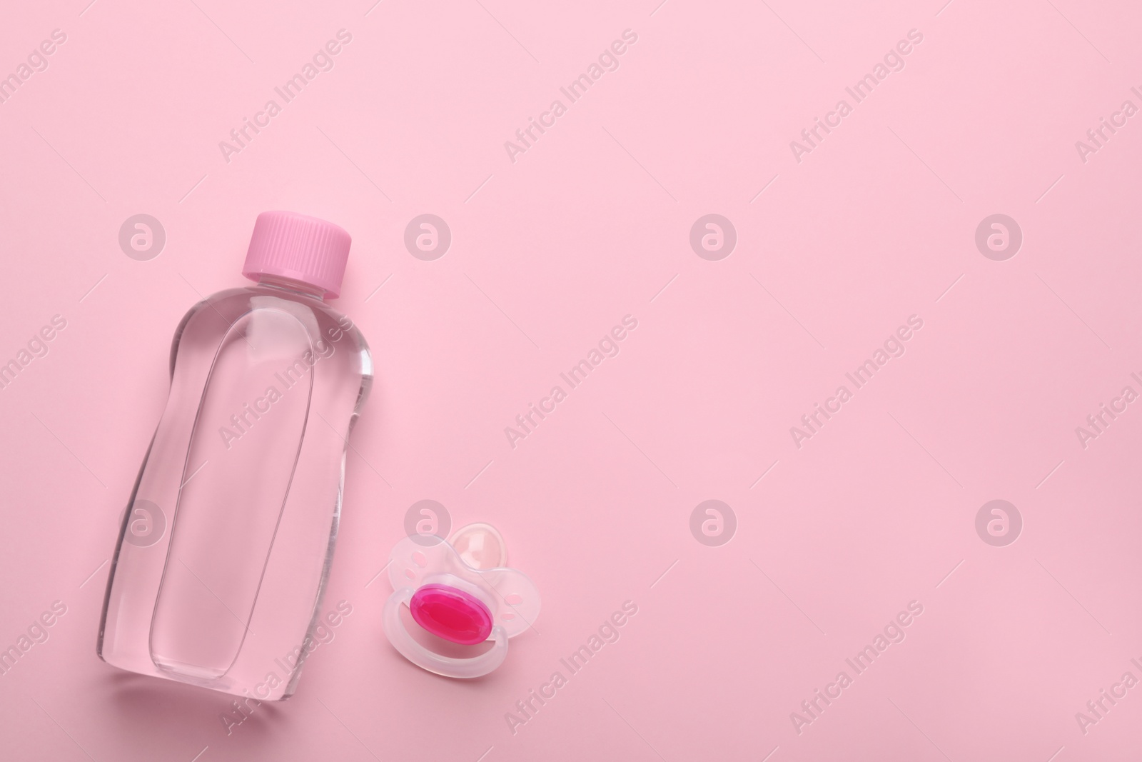 Photo of Bottle of baby oil and pacifier on pink background, flat lay. Space for text